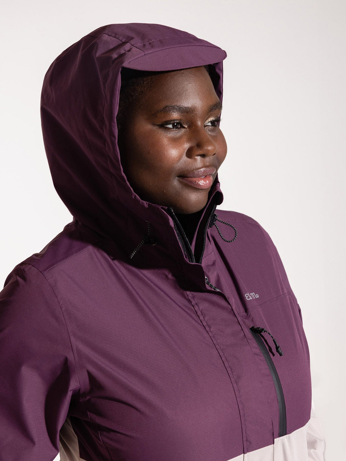 Ela Mo™ Regenjacke | Grape. Frau in einer rosa-lilafarbenen Regenjacke mit Kapuze auf dem Kopf.