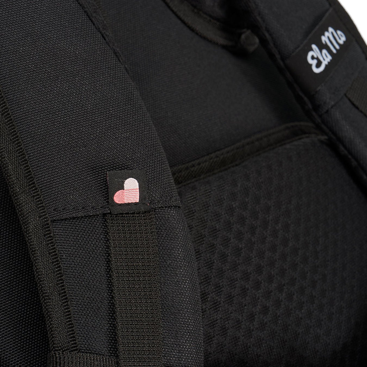 Ela Mo™ Everywhere Daypack | Black. Schulterriemen des schwarzen Rucksacks mit kleinen Herzchen und Herstellerlogo darauf.