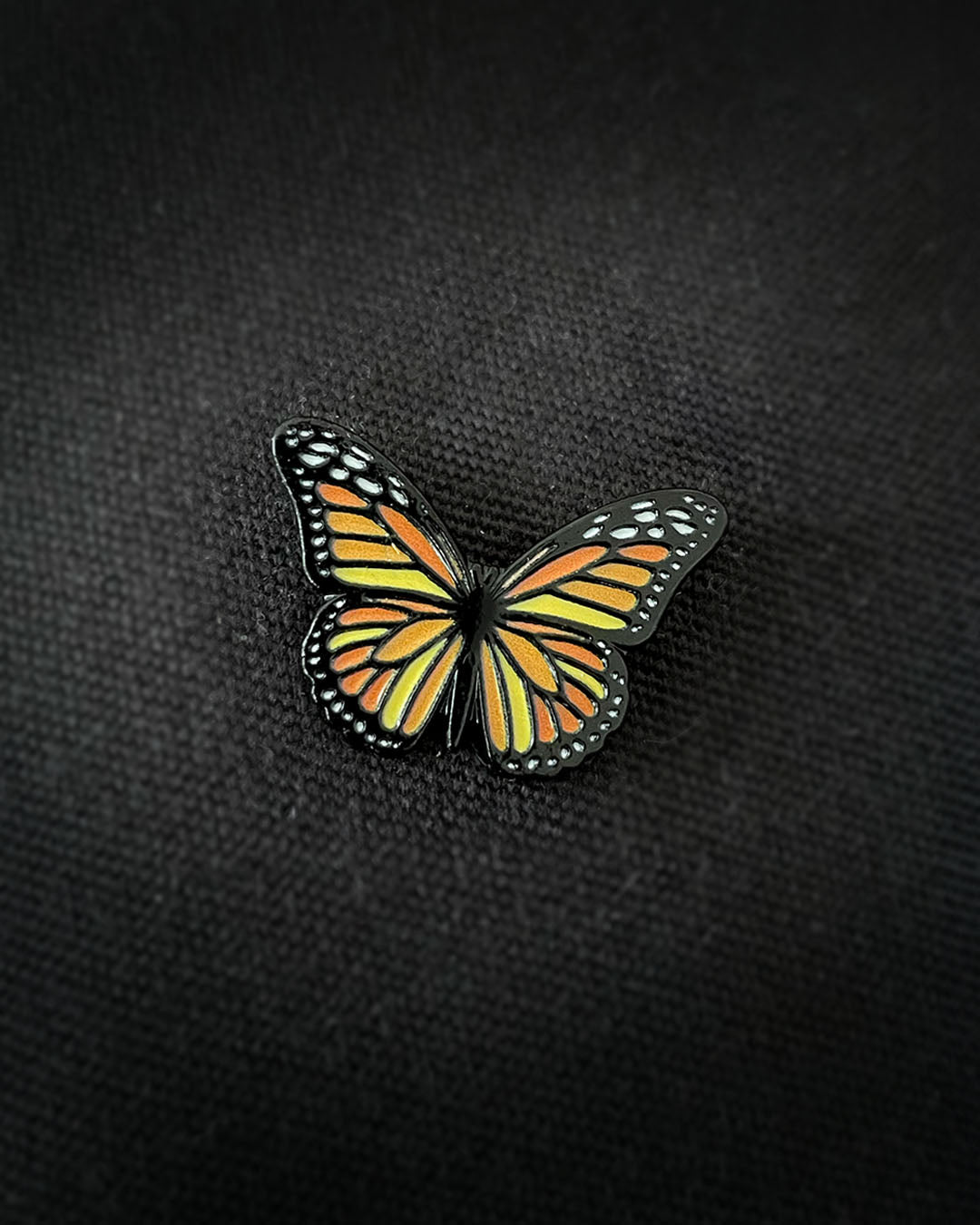 Ela Mo™ Mini Pin für Rucksäcke | Butterfly. Ein kleiner Schmetterlings-Pin auf dem schwarzen Rucksack befestigt.