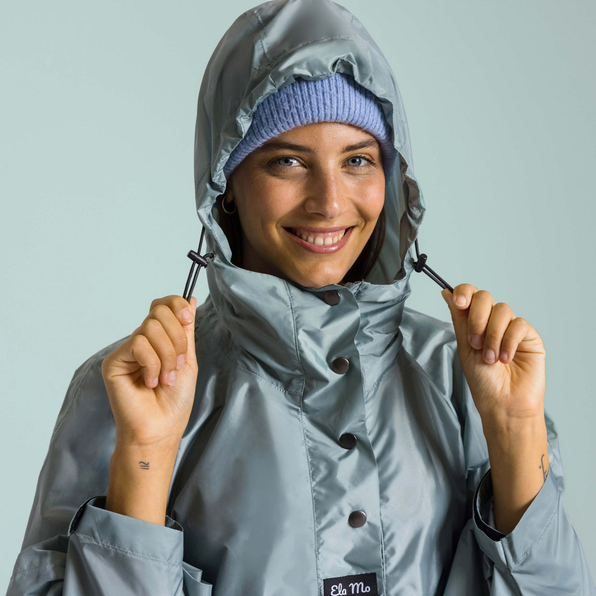Ela Mo™ Regenponcho | Mint. Eine Frau mit Regenponcho und Kapuze auf dem Kopf.
