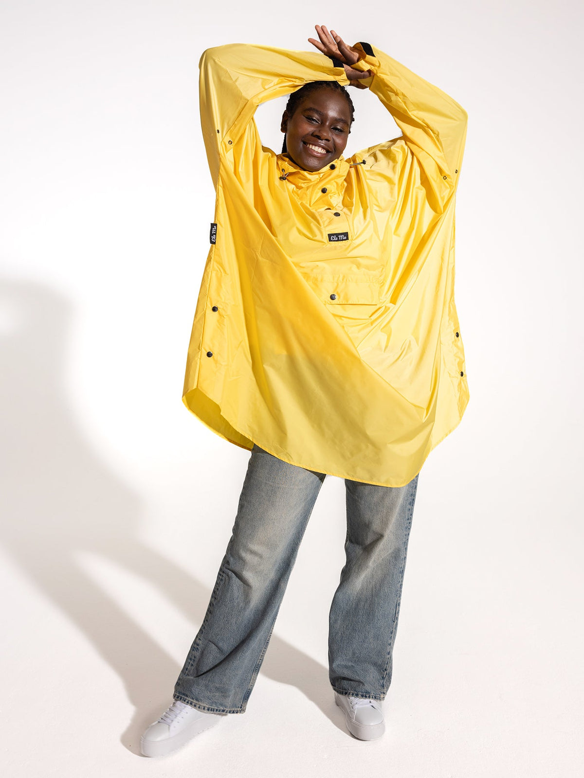 Ela Mo™ Regenponcho | Yellow. Eine Frau im Regenponcho, der ausreichend breit ist, auf weißem Hintergrund.