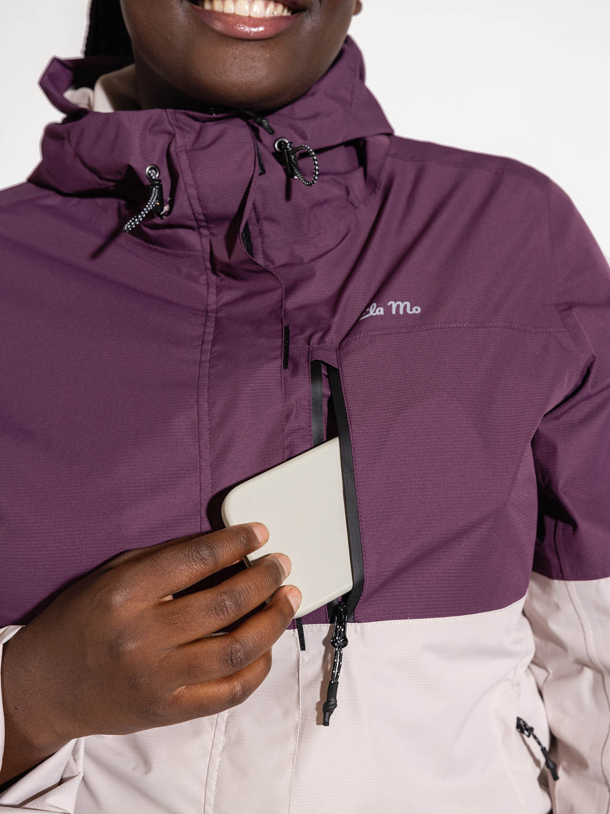 Ela Mo™ Regenjacke | Grape. Frau in  Regenjacke mit einer seitlichen Handytasche, die durch Reißverschluss geschützt ist.