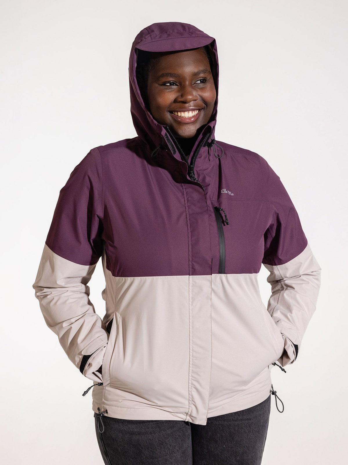 Ela Mo™ Regenjacke | Grape. Eine Frau in bequemer Regenjacke mit Reißverschluss und Kapuze auf dem Kopf.