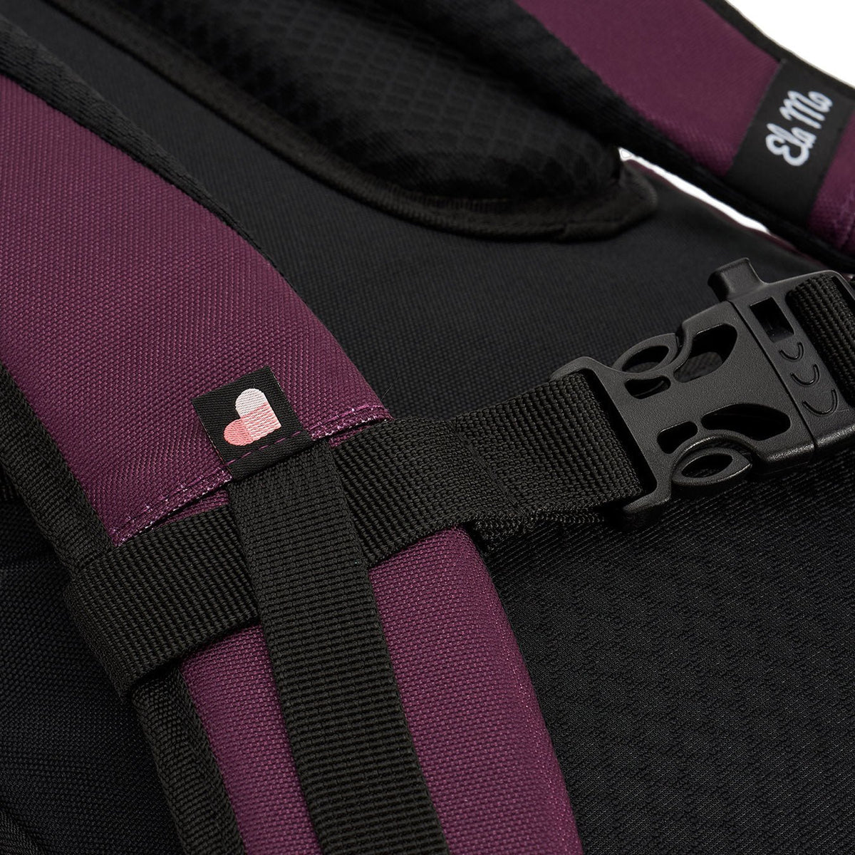 Ela Mo™ Everywhere Daypack | Grape. Schulterriemen mit Schnallenverschluss, Herstellerlogo und kleinem Herzdetail.