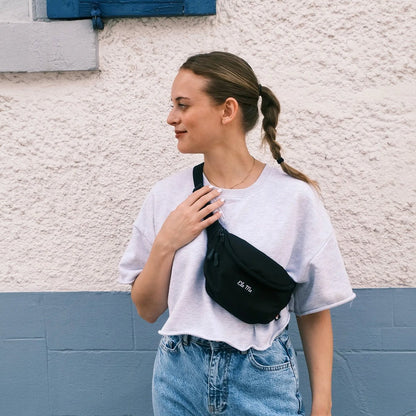 Ela Mo™ Hipbag  | Black. Eine Frau mit Hipbag an einem sonnigen Tag auf der Straße.