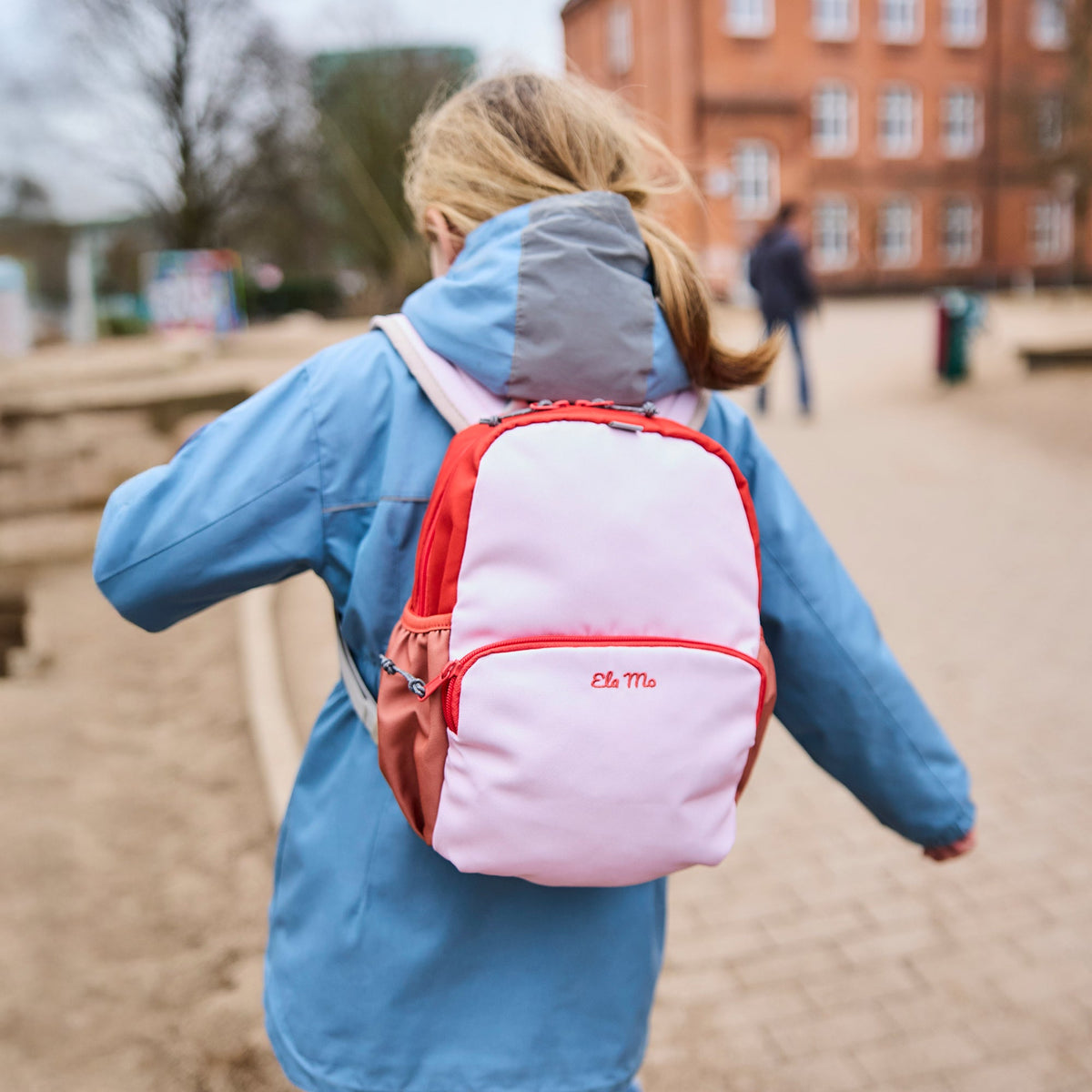 Ela Mo™ Kinderrucksack (3-6 Jahre) | Cotton Candy. Ein Mädchen trägt einen rosafarbenen Rucksack. Ein täglicher Style.