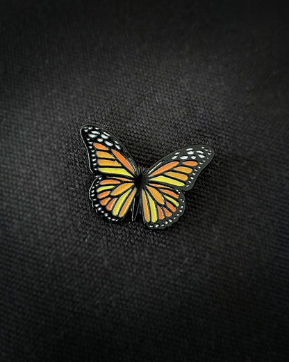 Ela Mo™ Mini Pin für Rucksäcke | Butterfly. Ein kleiner Schmetterlings-Pin auf dem schwarzen Rucksack befestigt.