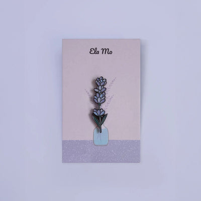 Ela Mo™ Mini Pin für Rucksäcke | Lavender. Ein kleiner Lavendel-Pin auf einer Karte befestigt, vor lila  Hintergrund.