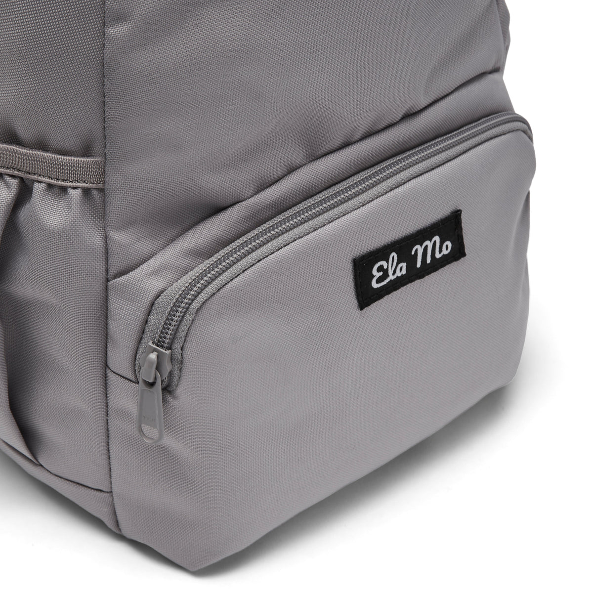 Ela Mo™ Mini Rucksack | Warm Grey. Außenfach mit Herstellerlogo auf der Vorderseite des Rucksacks.