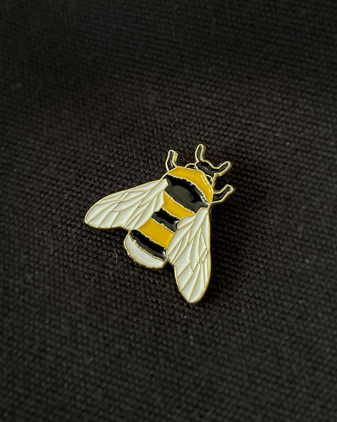 Ela Mo™ Mini Pin für Rucksäcke | Biene. Nahansicht eines kleinen Pins, befestigt auf dem schwarzen Rucksack.