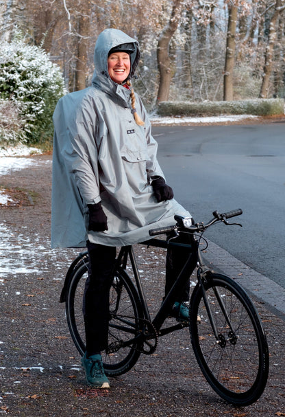 Ela Mo™ Regenponcho | Mint. Eine Frau mit Regenponcho und Fahrrad auf der Straße.