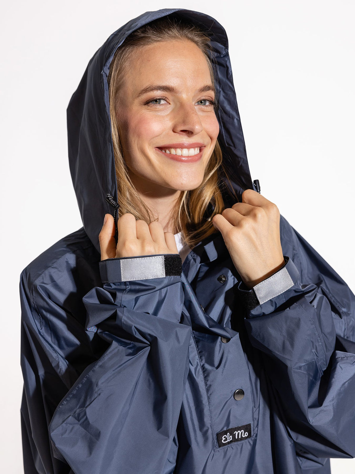 Ela Mo™ Regenponcho | Navy. Eine Frau im Regenponcho mit hohem Kragen und Kaputze auf weißem HIntergrund.