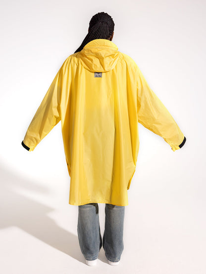 Ela Mo™ Regenponcho | Yellow. Eine Frau im Regenponcho mit Kapuze, Ansicht von hinten.