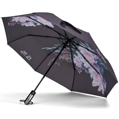 Ela Mo™ Taschenschirm | Beauty in Darkness. Ein schwarzer, geblümter Regenschirm mit Herstellerlogo darauf.
